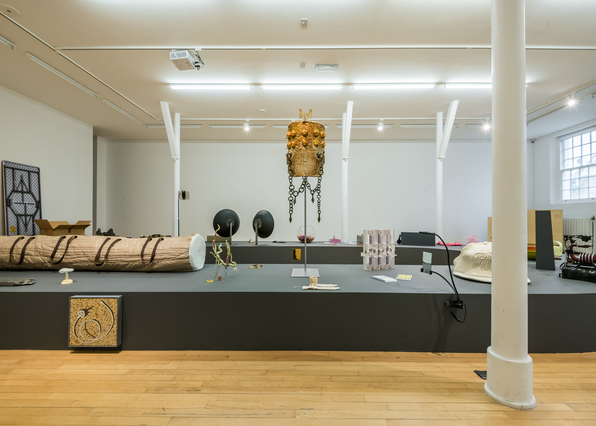 A low grey plinth mimicking a baggage reclaim conveyor belt supports a selection of small to medium sized sculptures. At the centre of the image are a pair of pale yellow socks, sitting on the plinth.