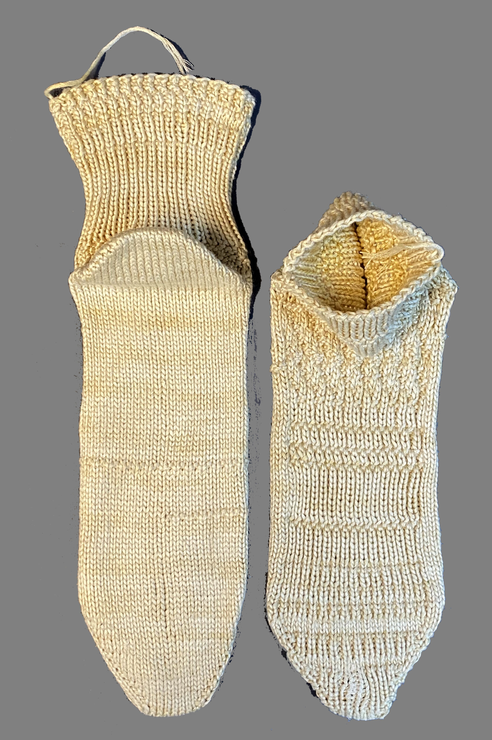 A pair of pale yellow socks on a grey background. They have a subtle striping and some offset rib texture bands. One is sitting up, the other is laying face down.